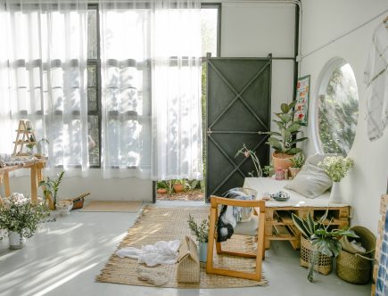 Apartamento com plantas e cortina branca na janela. Com móveis de madeira e uma porta preta de ferro.