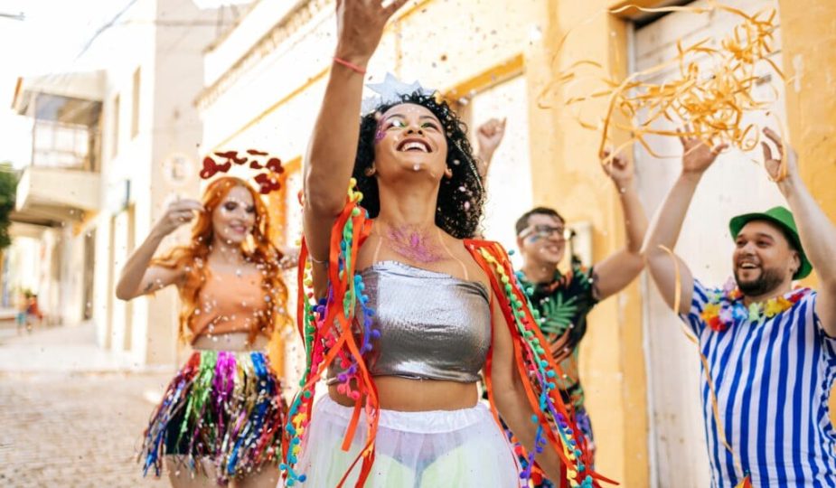 Foto de quatro foliões com maquiagem de carnaval, festejando muitos com confetes.