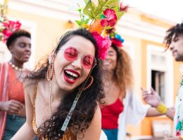 Foto de foliões usando fantasias de carnaval pela rua da cidade.