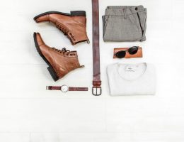 Foto de peças roupas de um guarda-roupa masculino, com camiseta branca, calça cinza, bota e cinto de couro.