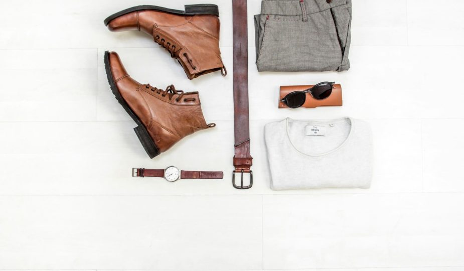 Foto de peças roupas de um guarda-roupa masculino, com camiseta branca, calça cinza, bota e cinto de couro.