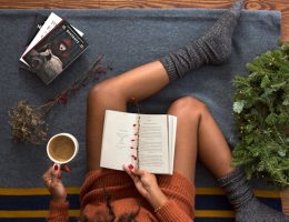 Foto de uma mulher no seu cantinho de leitura, com seu café e um bom livro.