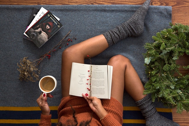Foto de uma mulher no seu cantinho de leitura, com seu café e um bom livro.
