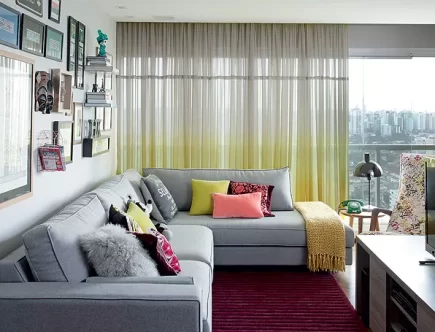 Foto de uma sala com sofá cinza com almofadas e mantas sobre e ele.