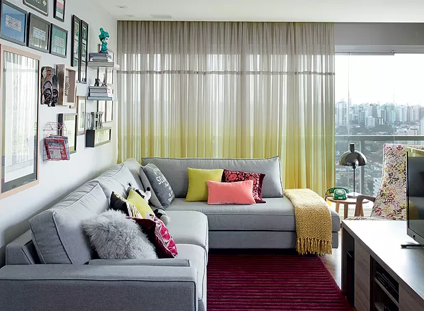 Foto de uma sala com sofá cinza com almofadas e mantas sobre e ele.