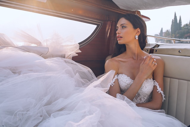 Foto de uma mulher dentro de um carro vestida com um vestido de noiva, olhando a paisagem.