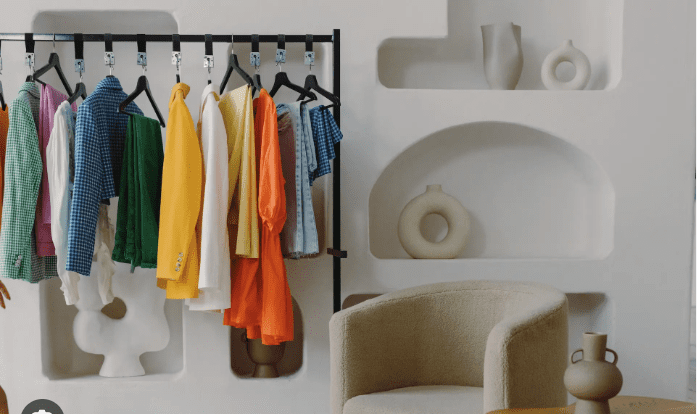 Foto de um guarda-roupa versátil com roupas coloridas e uma poltrona bege.