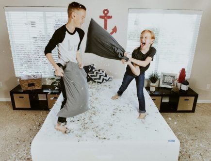 Foto de uma menina e um menino brincando em cima da cama em um quarto para dois filhos.