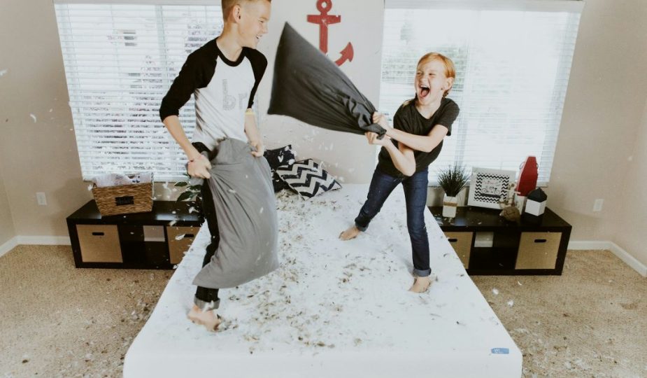 Foto de uma menina e um menino brincando em cima da cama em um quarto para dois filhos.